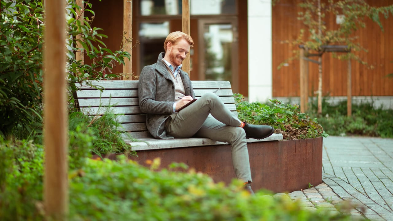 Mann sitter utendørs på en benk og smiler
